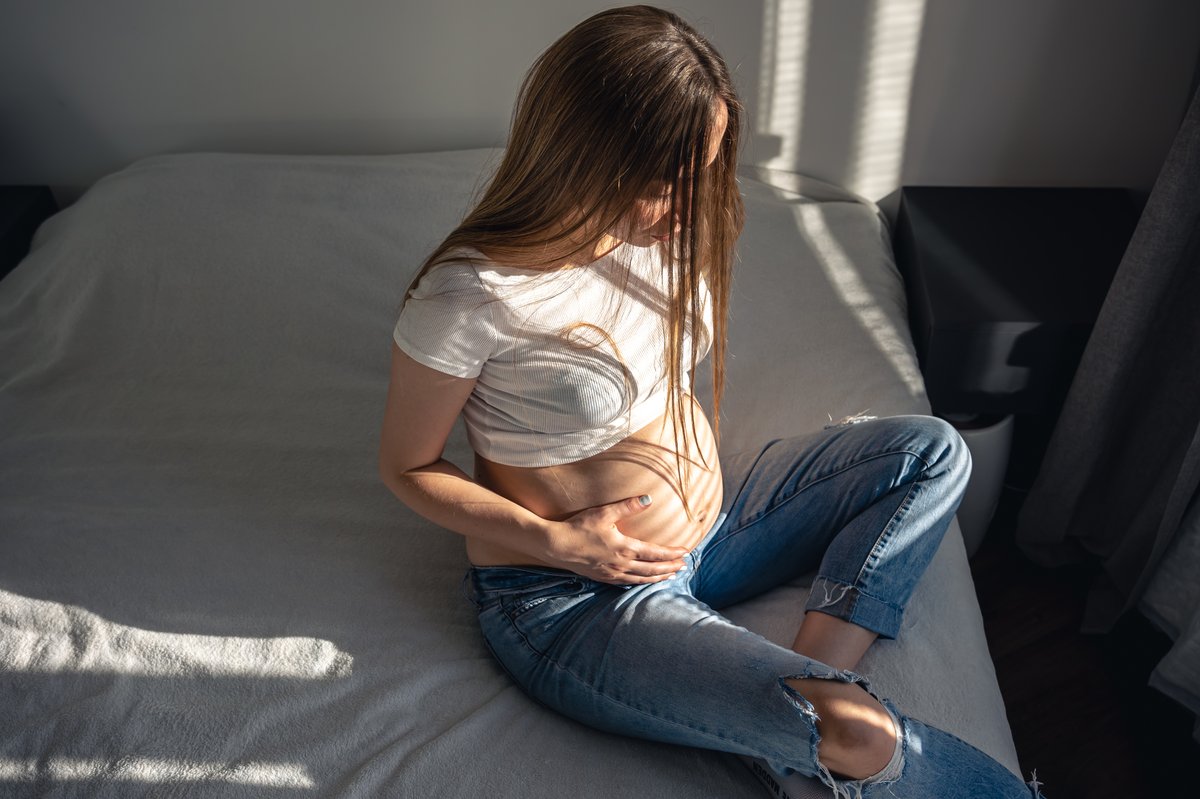 Mujer embarazada sentada junto a una ventana, con luz de mañana, sosteniendo su vientre